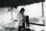Native American man examines clothing outside under shelter