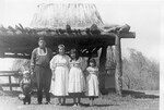 Native American family stands outside model hut