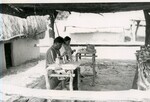 Native American man and woman work on crafts under shelter